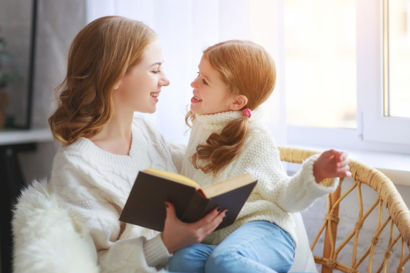 happy family mother reads book to child to daughter by window in winter morning